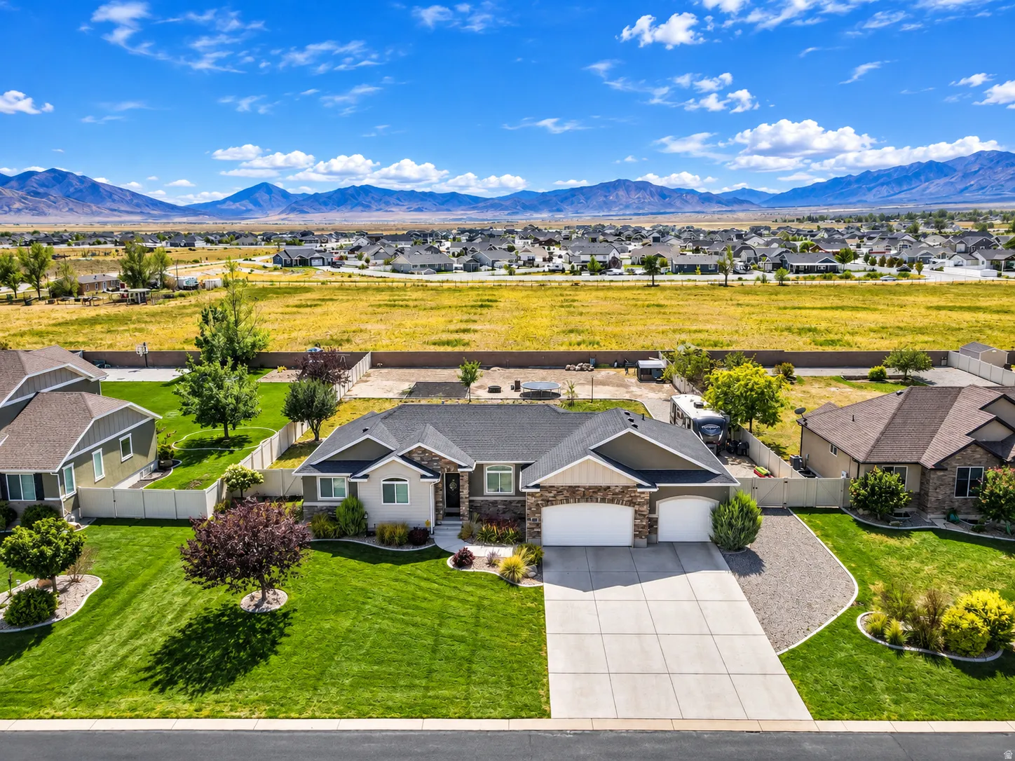 Ranch-style residence featuring a stone and stucco exterior, an attached three-car garage, a concrete driveway, and a manicured lawn with mature landscaping