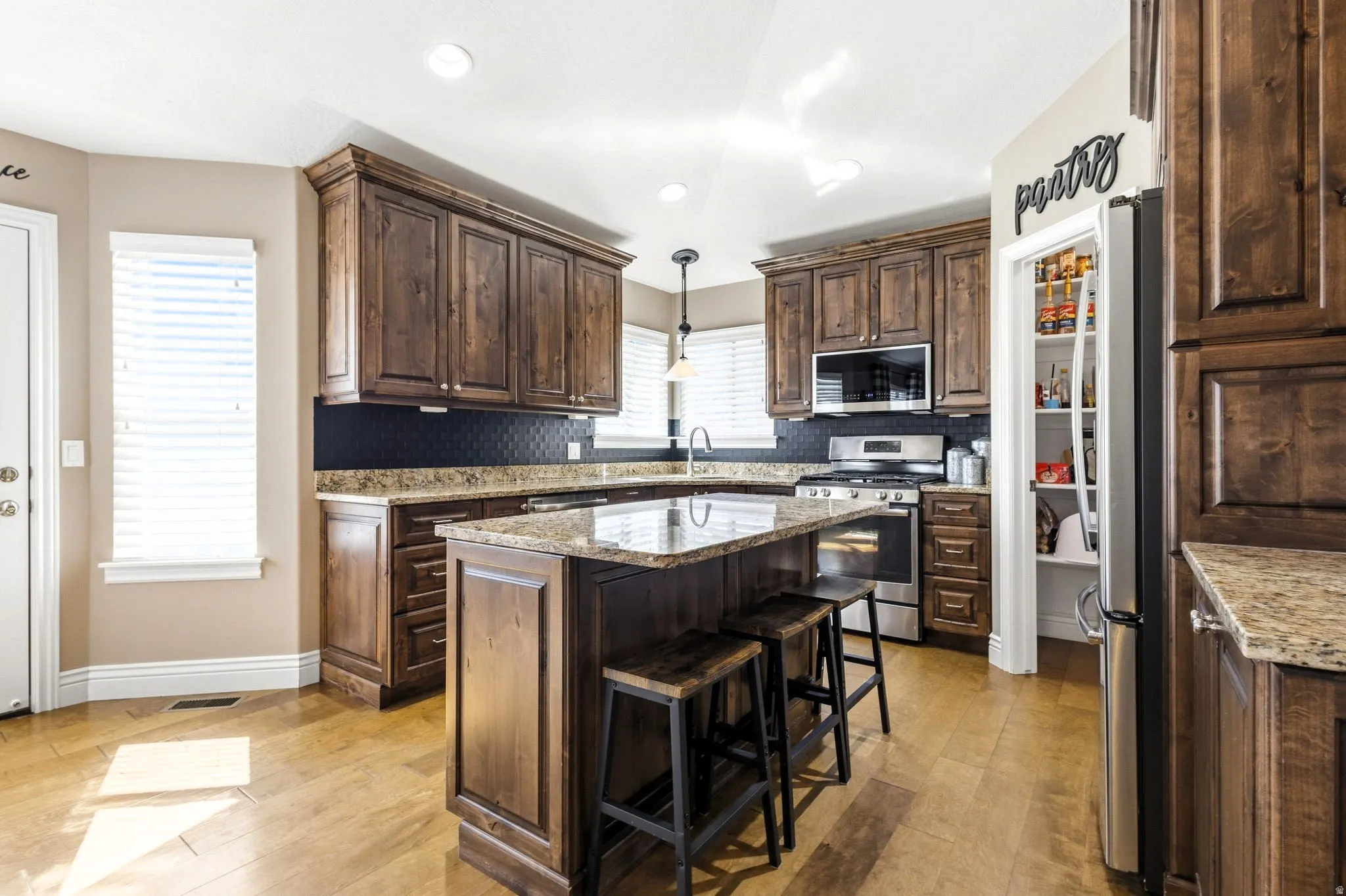 Wood-finish flooring with a kitchen island, granite countertops, and dark wood cabinetry