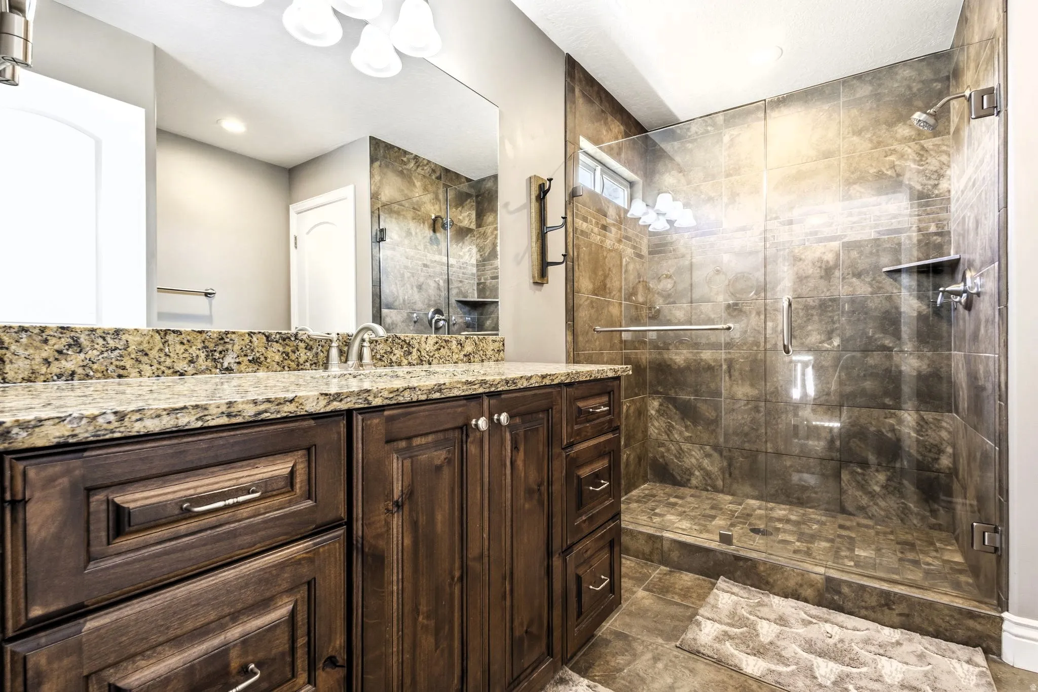 Primary bathroom with dark wood vanity with a light-toned granite countertop, a full-width mirror, and a glass-enclosed shower featuring tiled walls and a built-in shower niche