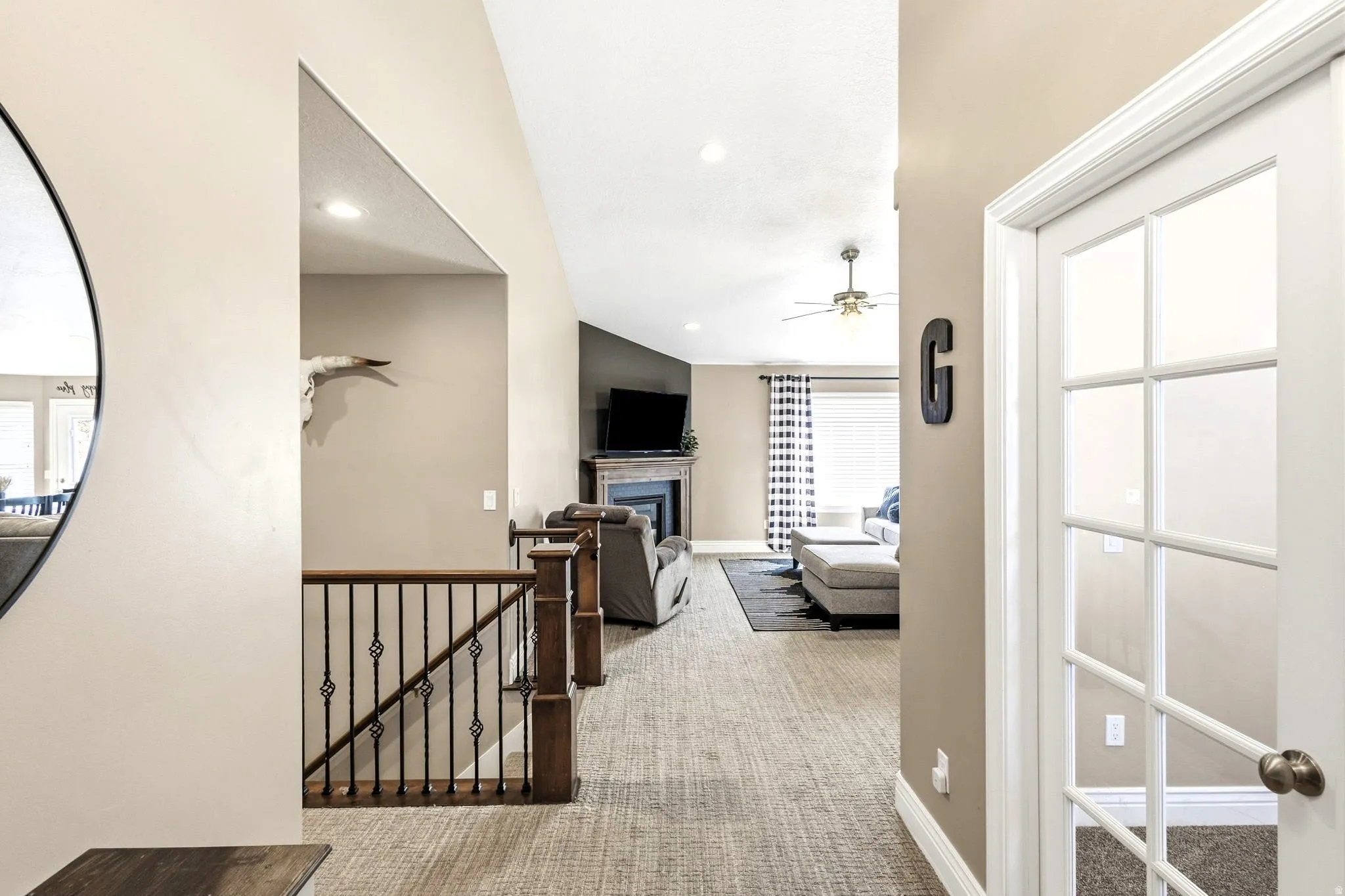 Vaulted ceiling, recessed lighting, ceiling fan, wood-finish staircase railing with decorative metal balusters, and a fireplace with a mantel