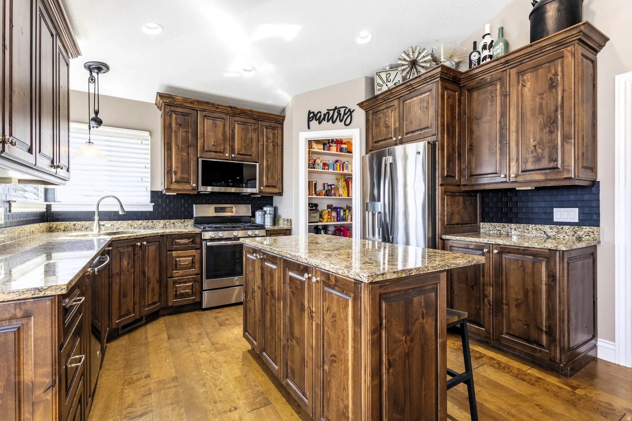 Kitchen featuring wood-finish flooring, dark wood cabinetry, granite countertops, stainless steel appliances, and a walk-in pantry