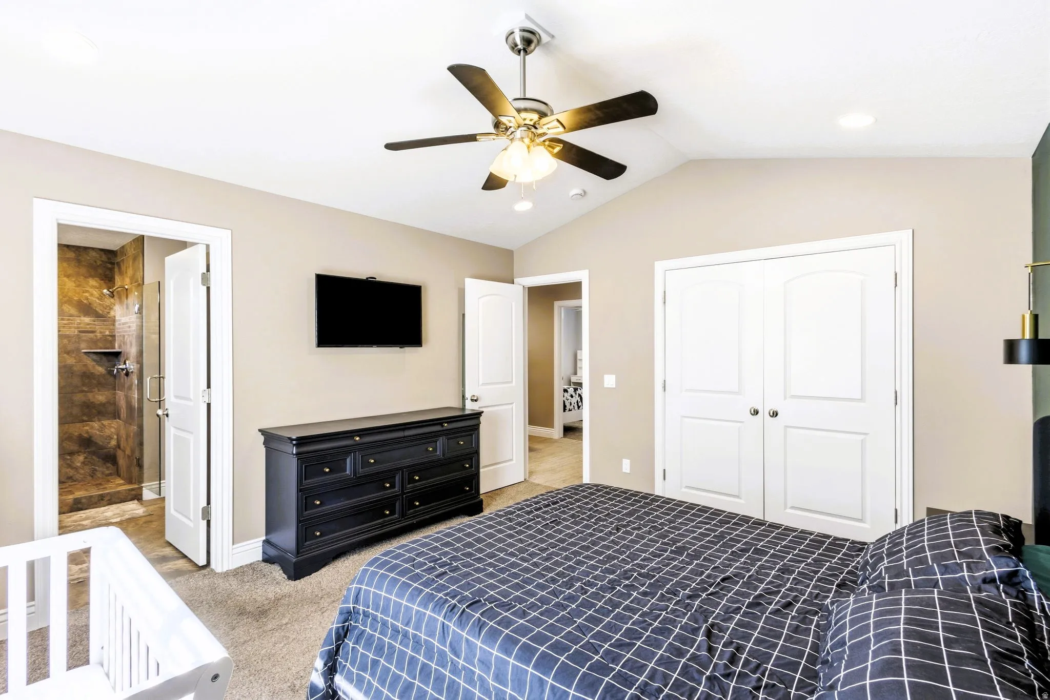 Primary bedroom with vaulted ceiling and ceiling fan, carpeted flooring, double-door closet, and an attached bathroom with a tiled shower.