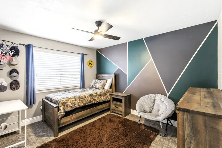 Bedroom #2 with accent wall with geometric design, ceiling fan with integrated lighting, window with blinds, wood-finish bed frame, and wood-finish nightstand
