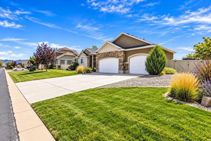 Stucco and stone facade, arched garage doors, concrete driveway, manicured lawn, and established landscaping with plenty of RV parking behind gate.