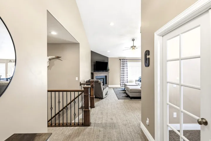 Vaulted ceiling, recessed lighting, ceiling fan, wood-finish staircase railing with decorative metal balusters, and a fireplace with a mantel