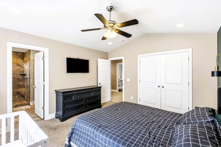 Primary bedroom with vaulted ceiling and ceiling fan, carpeted flooring, double-door closet, and an attached bathroom with a tiled shower.