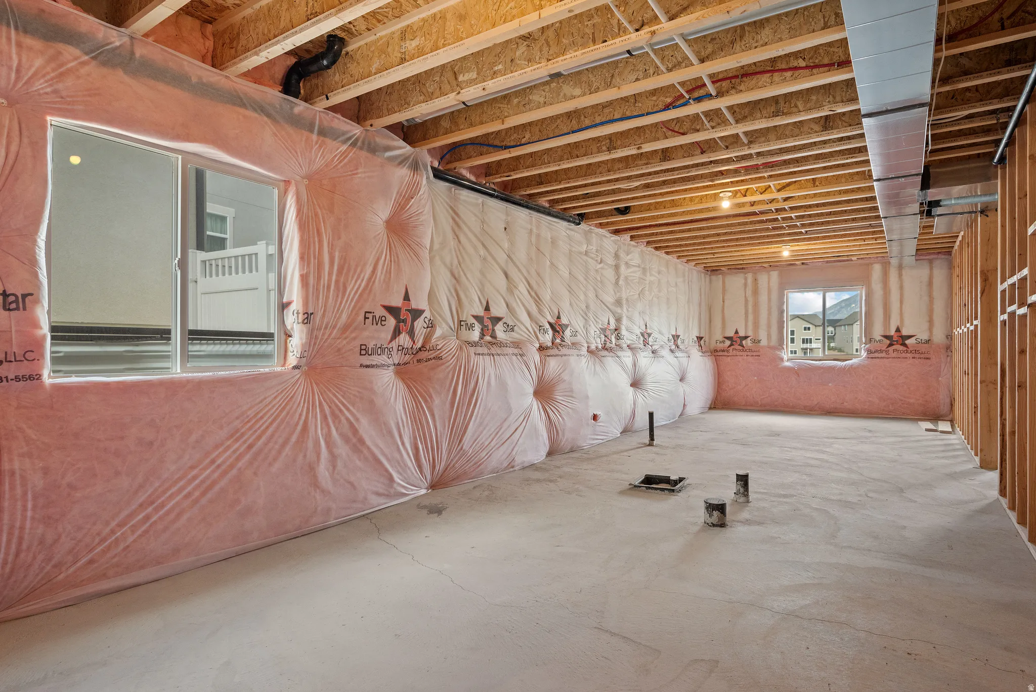 Unfinished basement featuring exposed wood joists, concrete flooring, perimeter insulation, and multiple windows