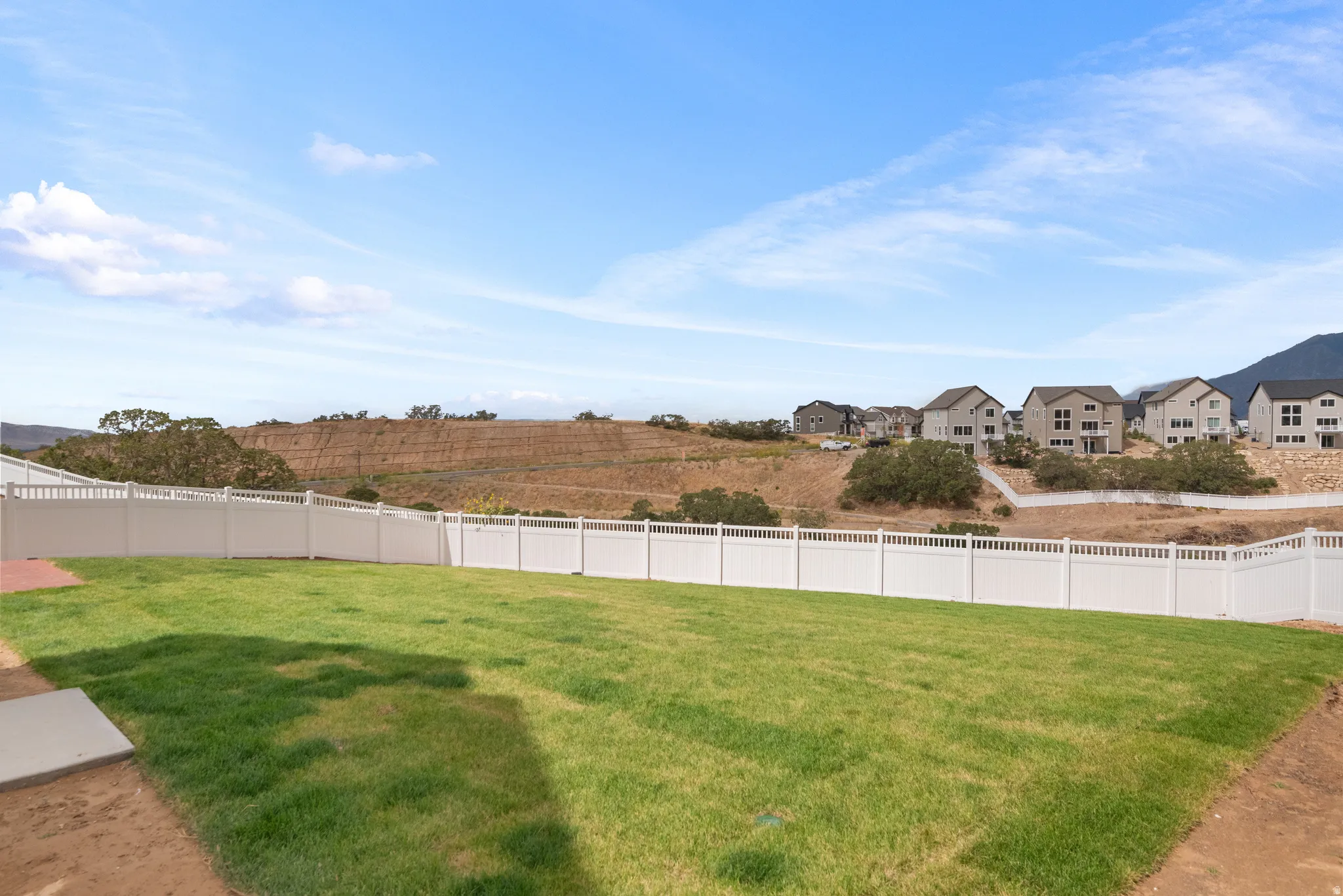Expansive backyard featuring a manicured lawn, white privacy fencing, and a concrete patio pad