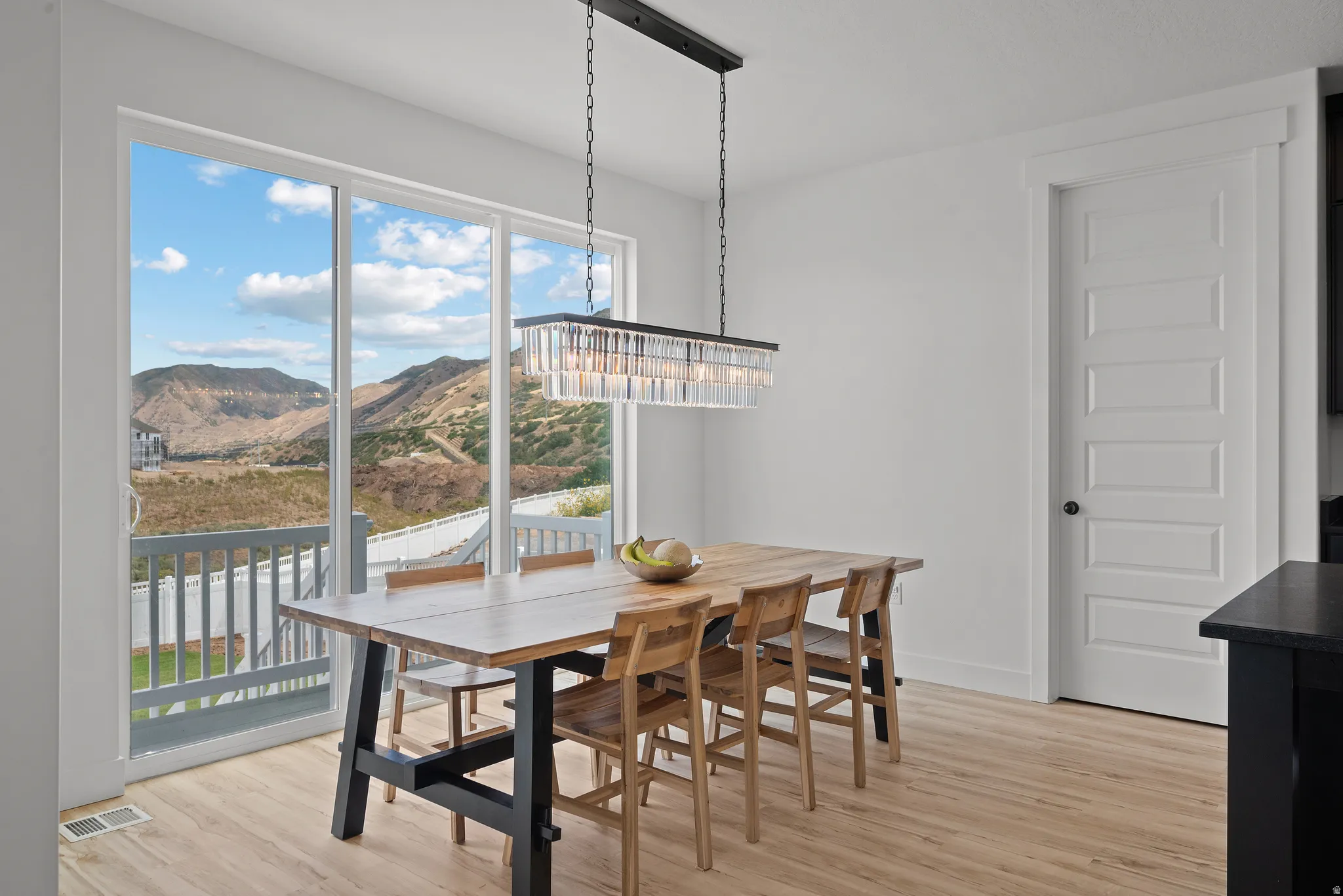 Sliding glass door leading to a balcony, featuring a linear chandelier with glass elements, light wood-finish flooring, and a five-panel interior door