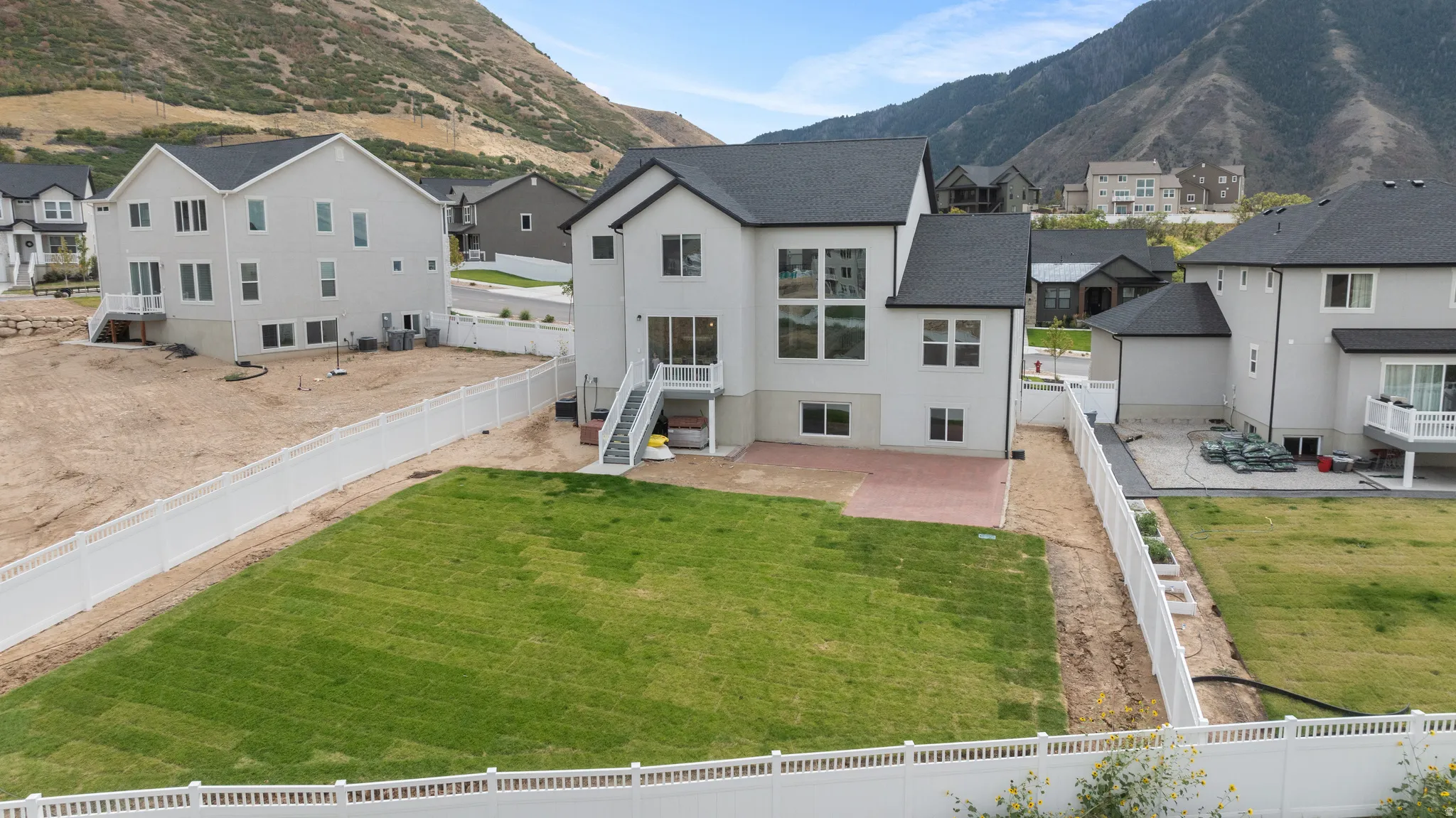 Expansive backyard featuring a manicured lawn, white privacy fencing, and brick paver patio