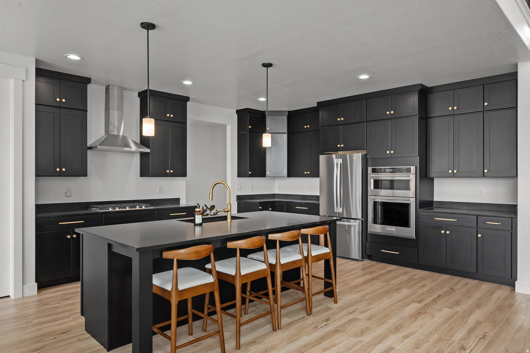 Well-appointed kitchen featuring dark cabinetry, stainless steel appliances, an expansive island, and wood-finish flooring