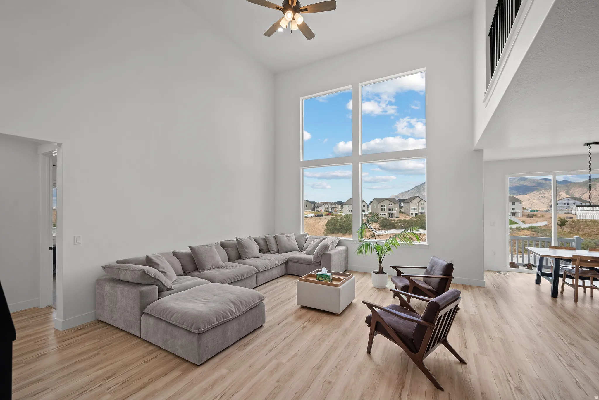 Vaulted ceilings, expansive window wall, wood-finish flooring, ceiling fan, and balcony with metal railing