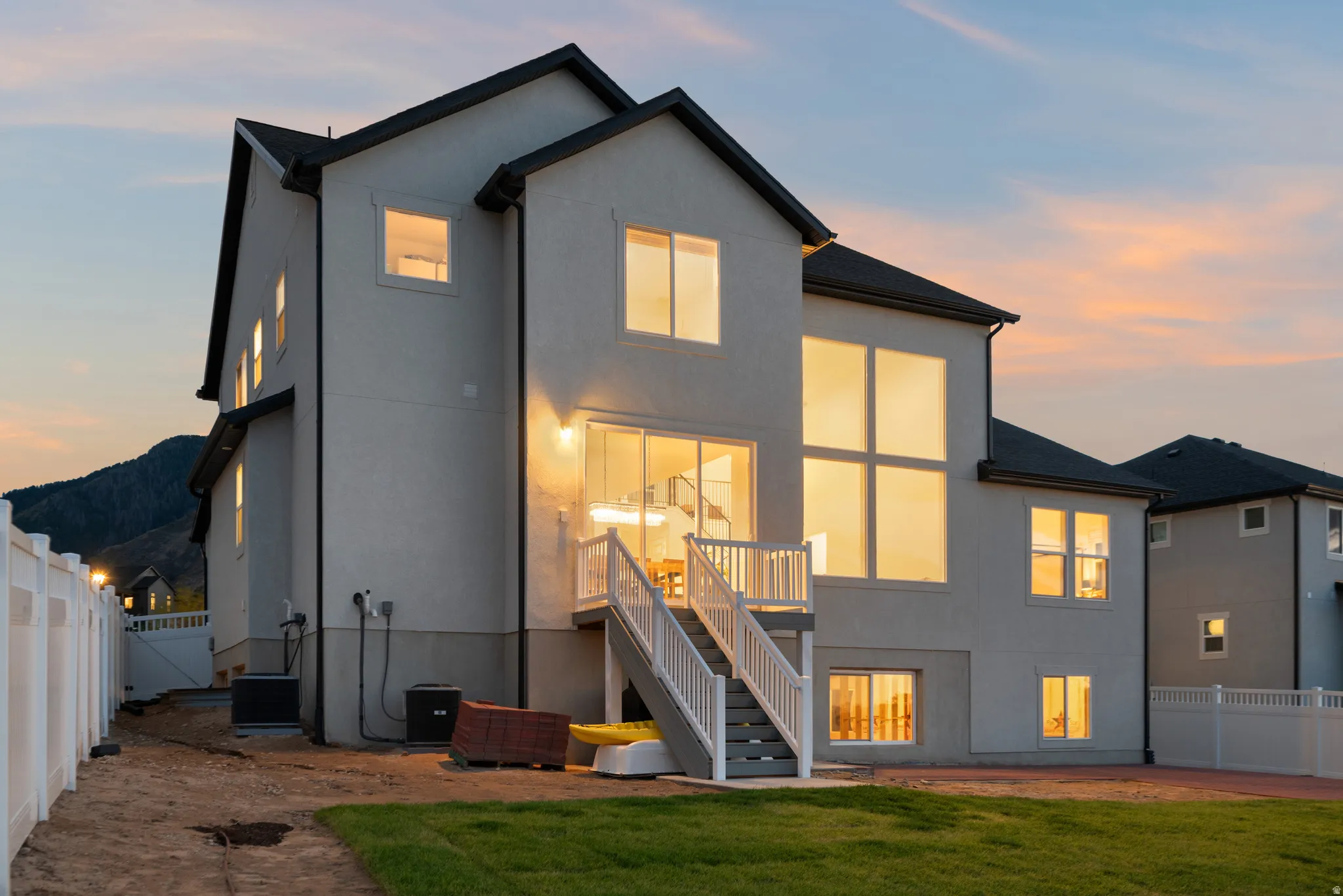 Stucco exterior with multiple large windows, a prominent deck with stairs, a white privacy fence, and a manicured lawn area