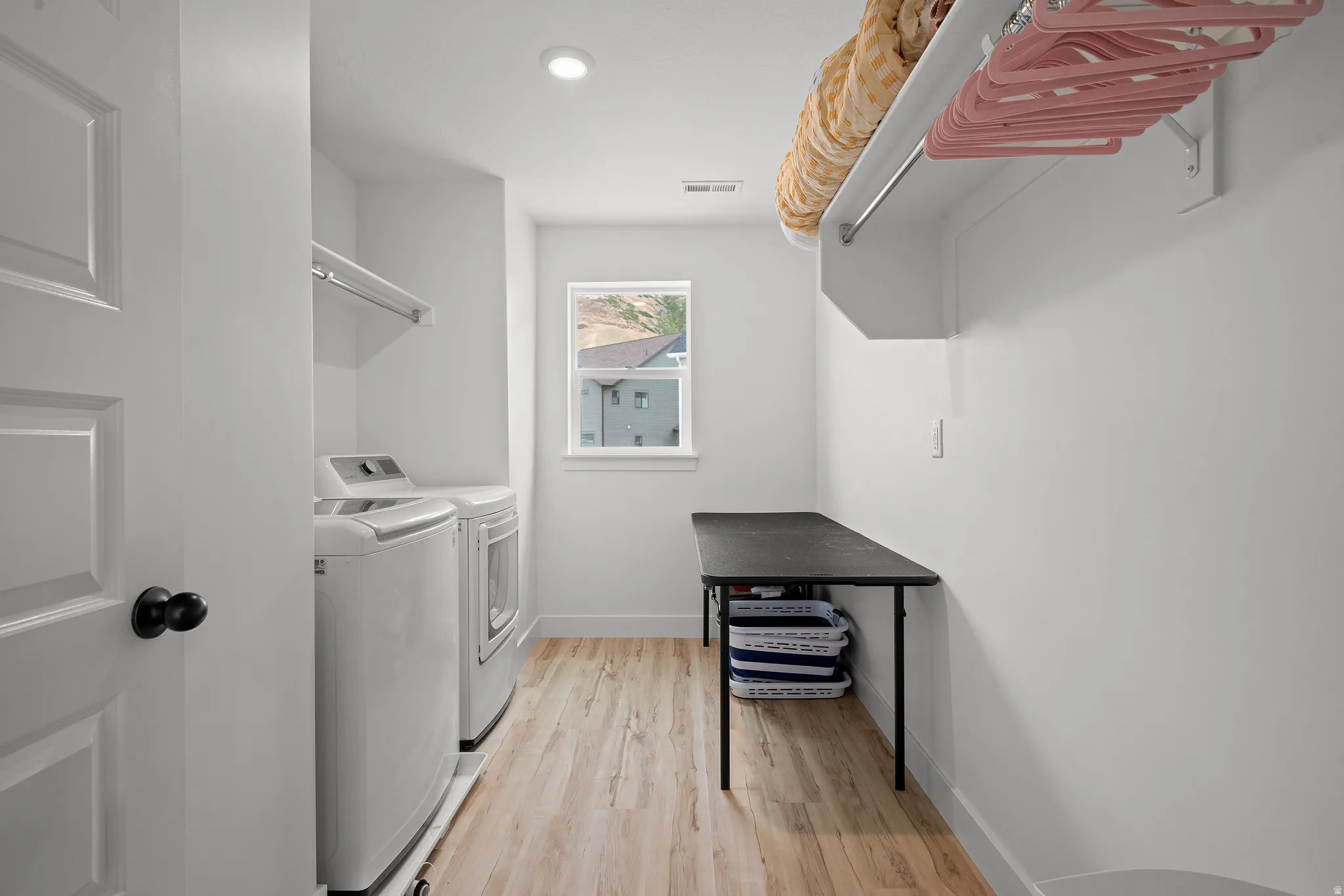 Laundry room featuring wood-finish flooring, a window, and an overhead shelf with a hanging rod