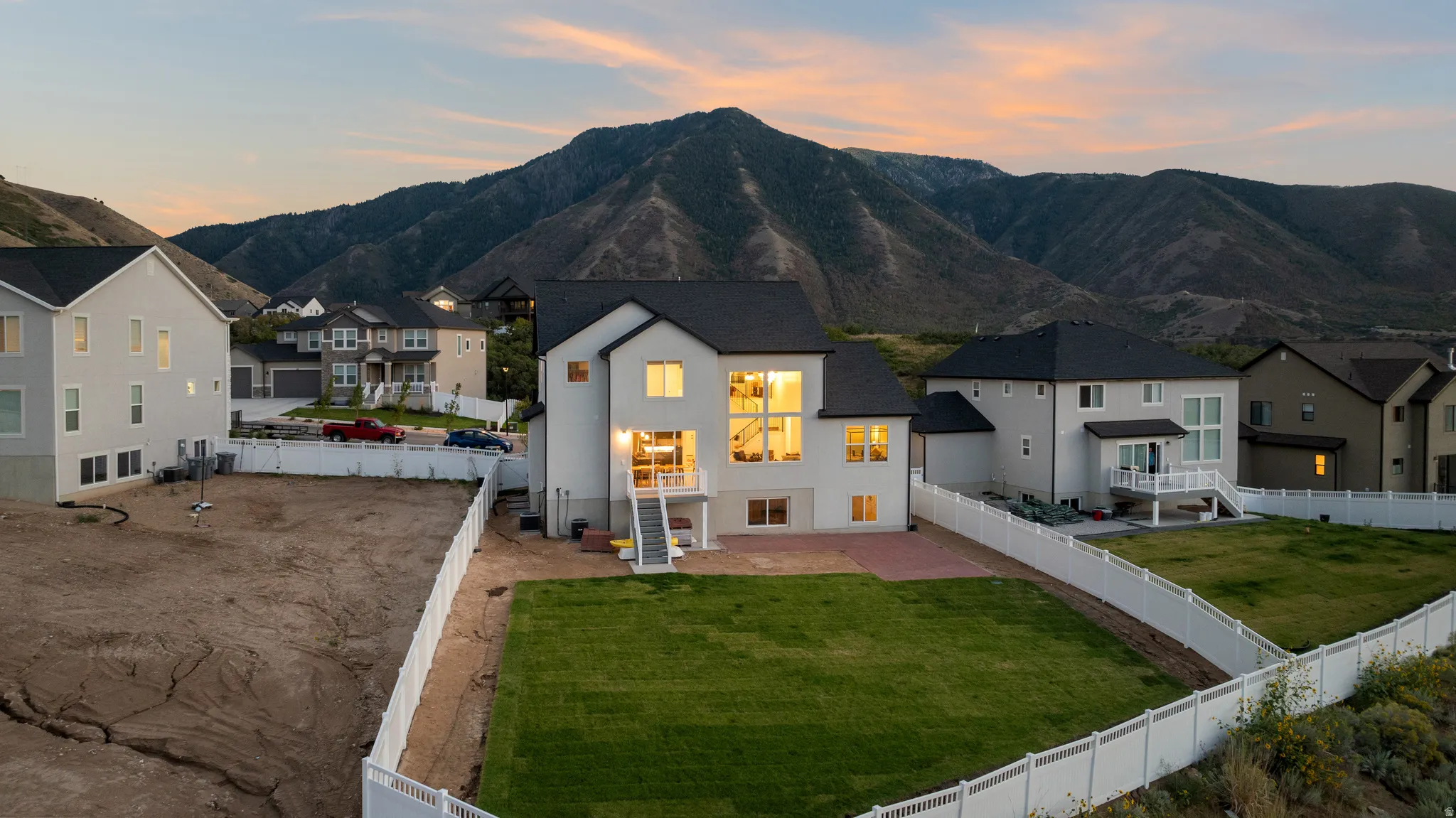 Contemporary two-story residence with a dark roof and white exterior, featuring large windows and a rear deck with stairs to a manicured lawn
