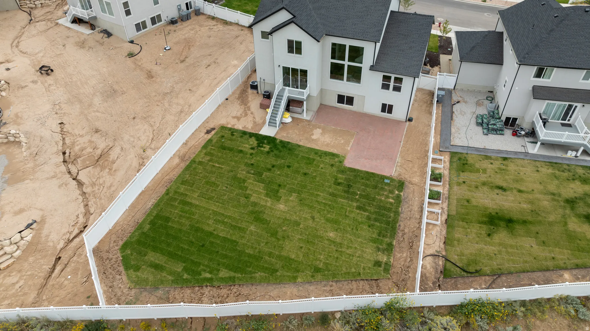 Expansive backyard featuring a newly laid lawn, a white vinyl fence, and a brick paver patio