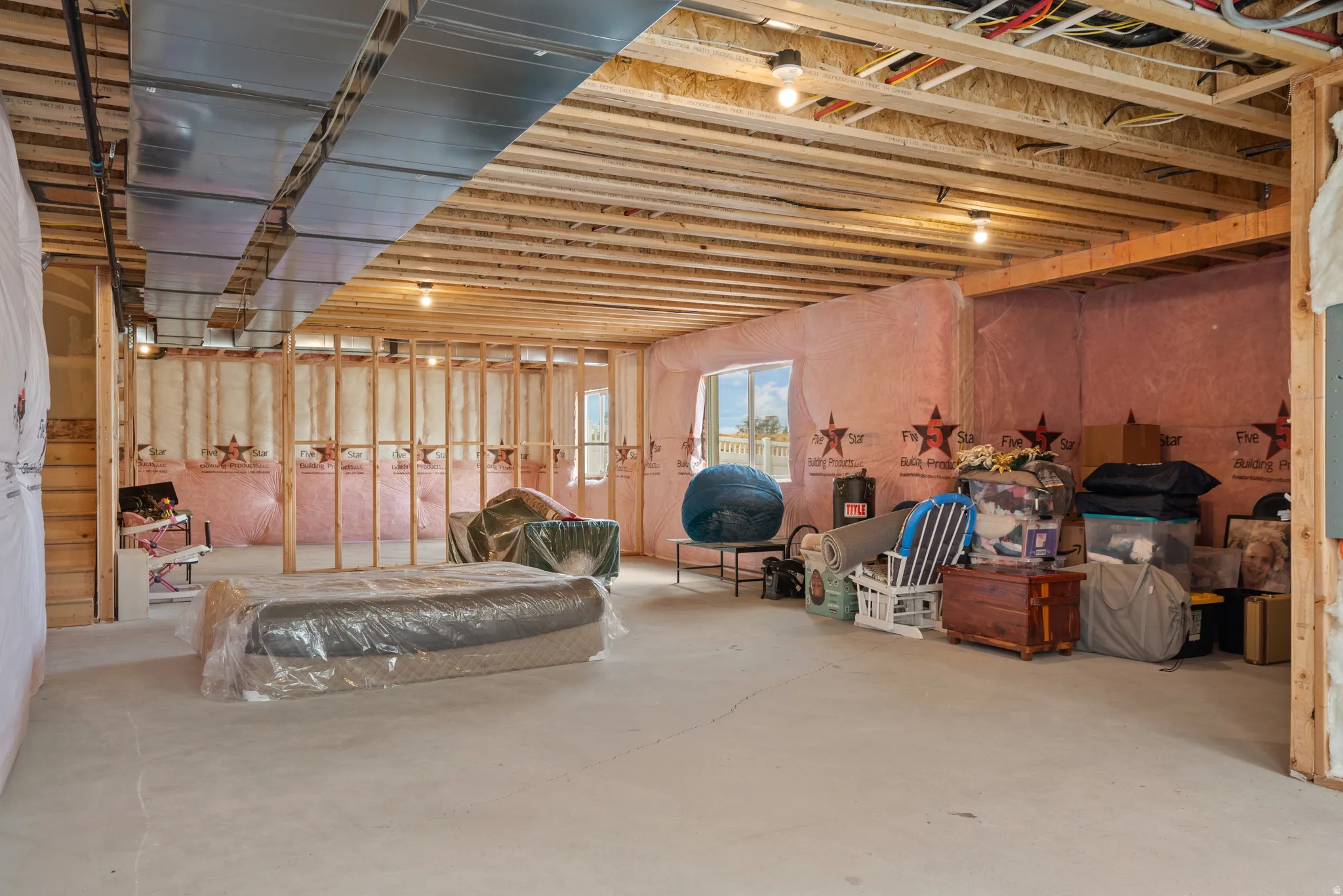 Unfinished basement with exposed wood framing, concrete flooring, and an egress window