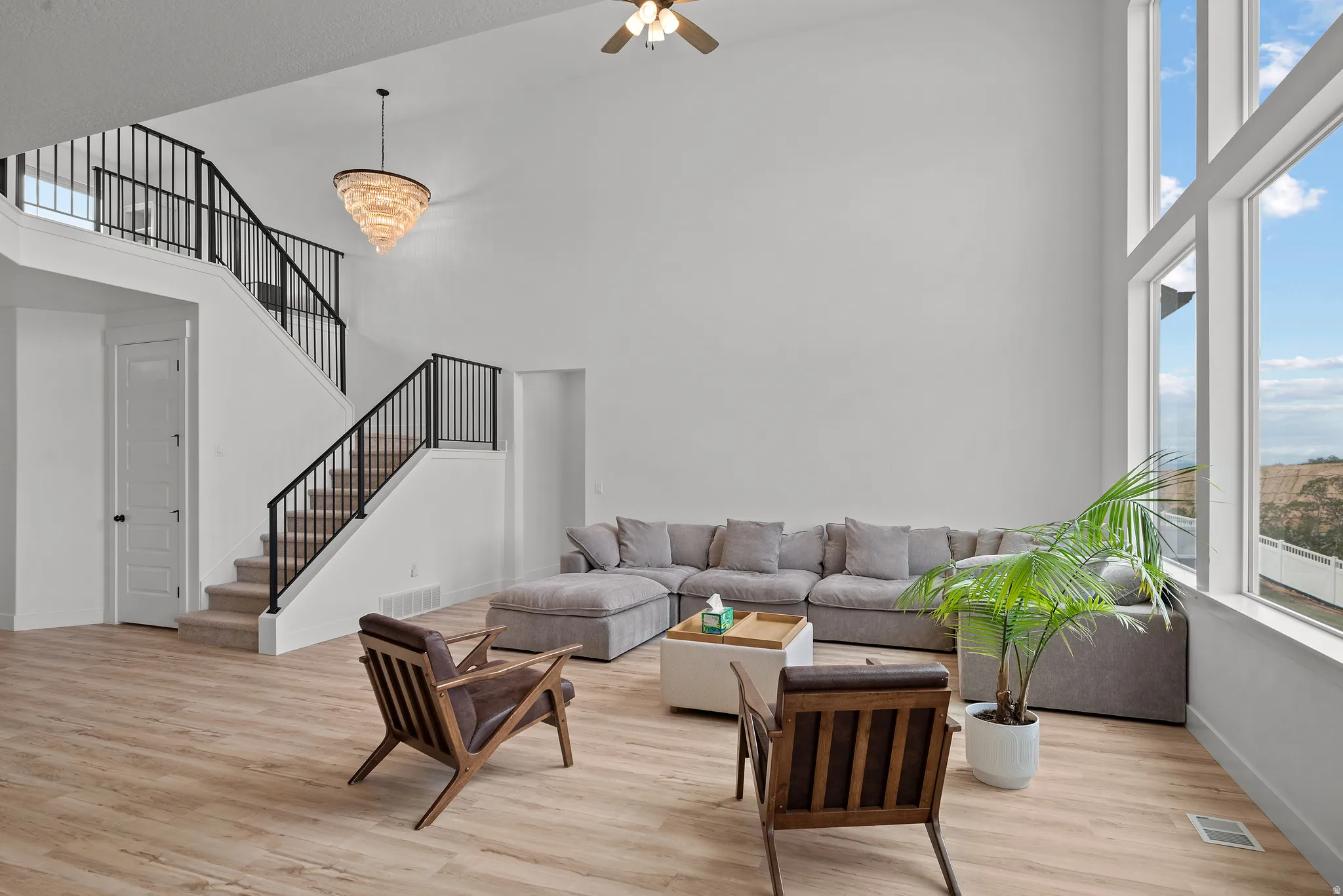 High ceilings, wood-finish flooring, two-story window wall, chandelier, and a staircase with black metal balusters