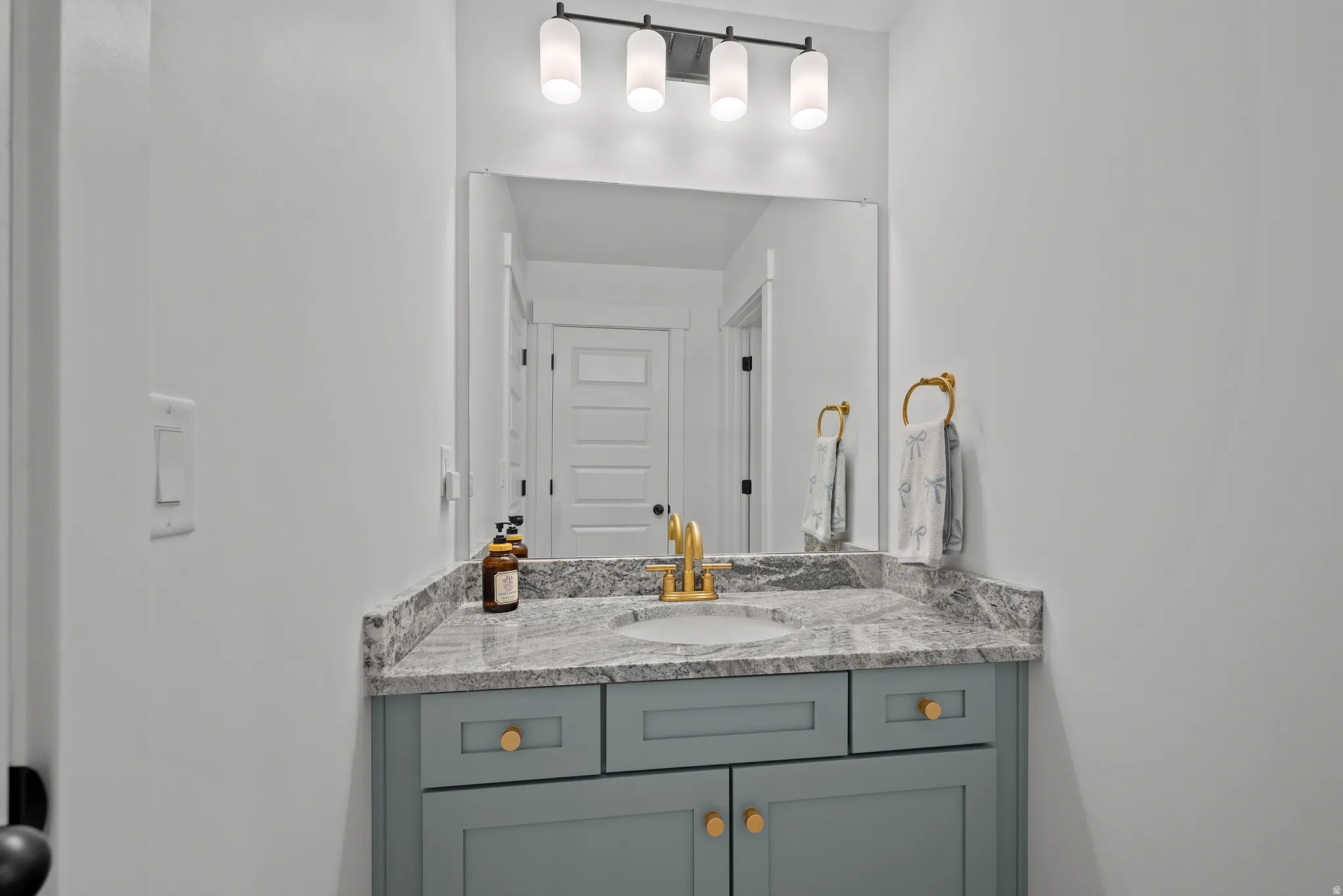 Light gray vanity with gold hardware, gray patterned countertop, undermount sink with gold-finish faucet, and rectangular mirror