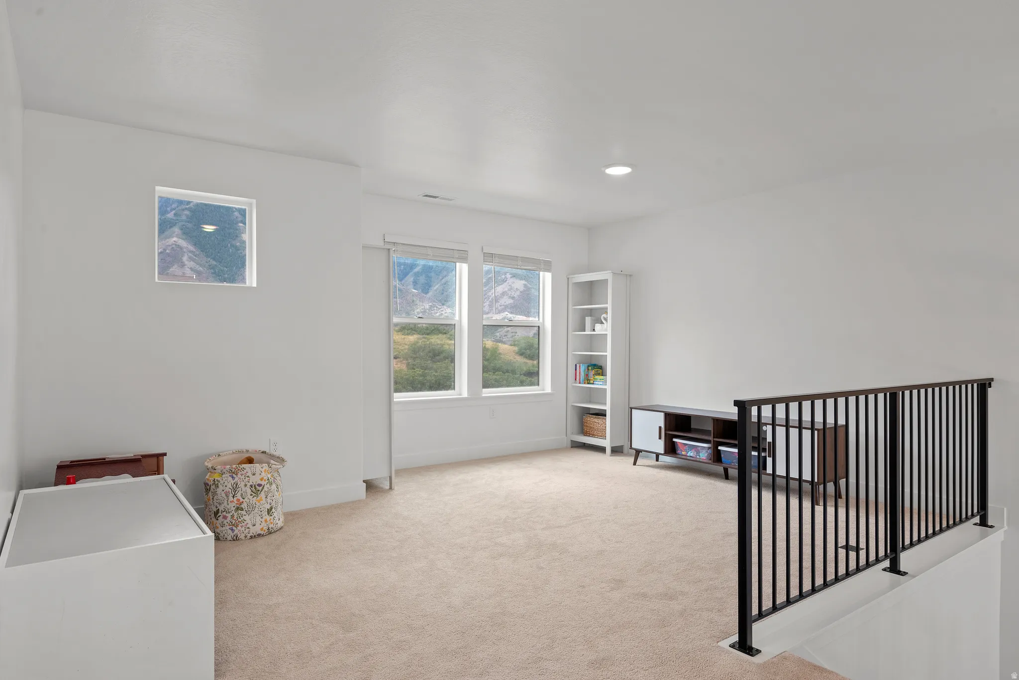 Carpeted open-concept space featuring multiple windows, recessed lighting, and a black metal railing