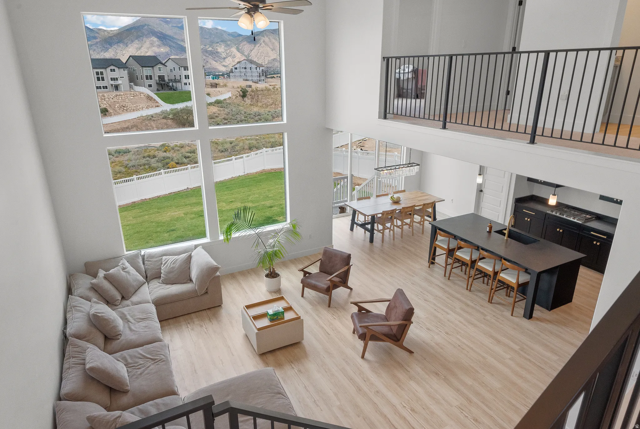 Two-story living area with expansive picture windows, wood-finish flooring, and an open balcony overlooking the space