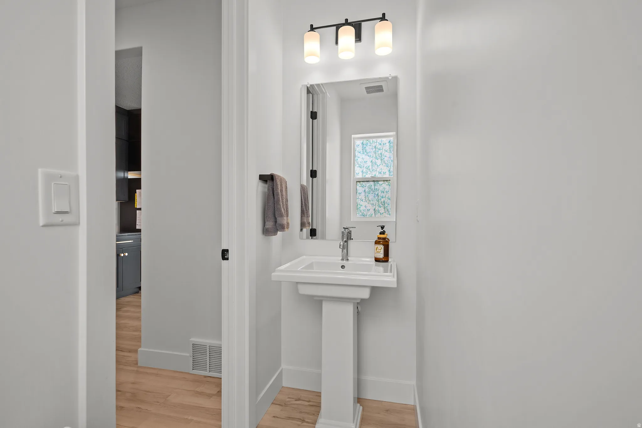 Pedestal sink with chrome faucet, rectangular wall mirror, and matte black vanity light fixture