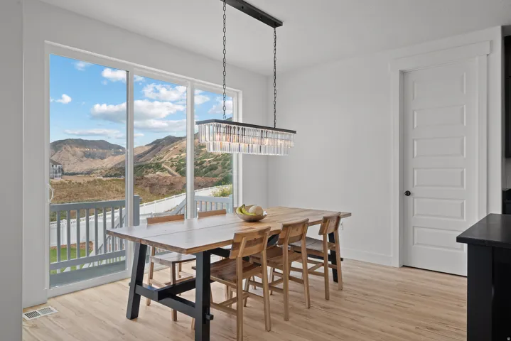 Sliding glass door leading to a balcony, featuring a linear chandelier with glass elements, light wood-finish flooring, and a five-panel interior door