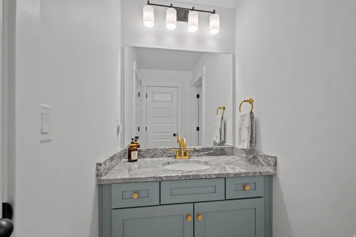Light gray vanity with gold hardware, gray patterned countertop, undermount sink with gold-finish faucet, and rectangular mirror