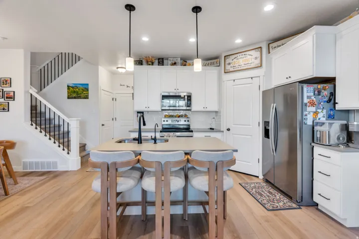 Modern kitchen featuring wood-finish flooring, white cabinetry, a built-in stainless steel oven, a stainless steel refrigerator, and a kitchen island with an integrated sink