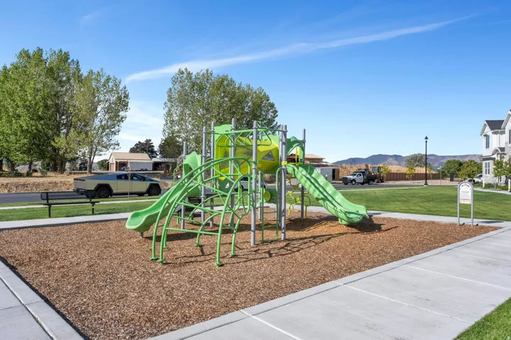 Community playground with green play structures, wood chip surfacing, and adjacent green space