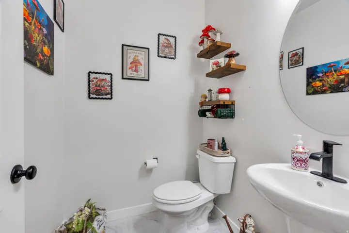 White pedestal sink with a black faucet, white toilet, and floating wood shelves