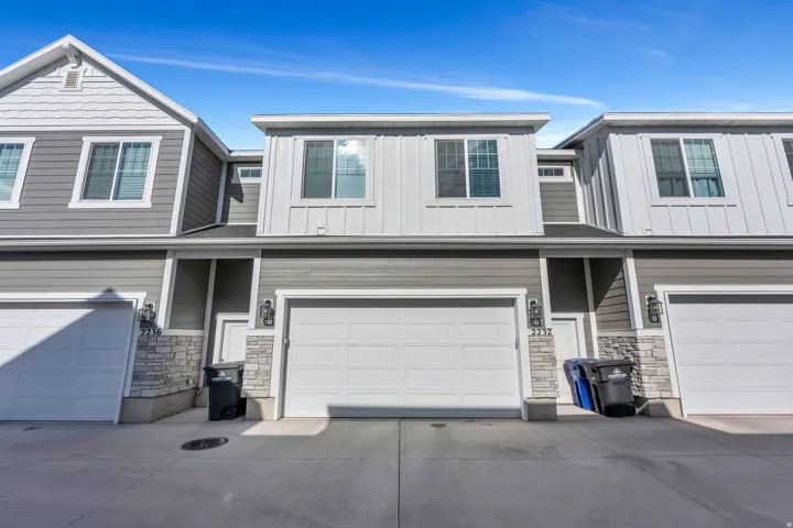 Contemporary exterior featuring gray siding, white board and batten accents, stone veneer detailing, and white garage doors