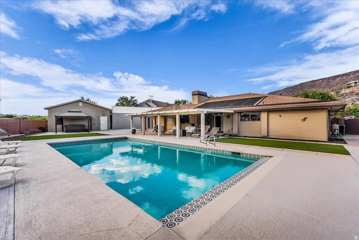 Expansive backyard featuring a rectangular swimming pool with decorative tile border, a covered patio, and a separate structure with an additional covered area