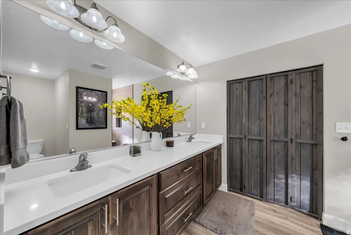 Double vanity with integrated sinks, white countertops, wood-finish flooring, and dark wood-paneled closet doors