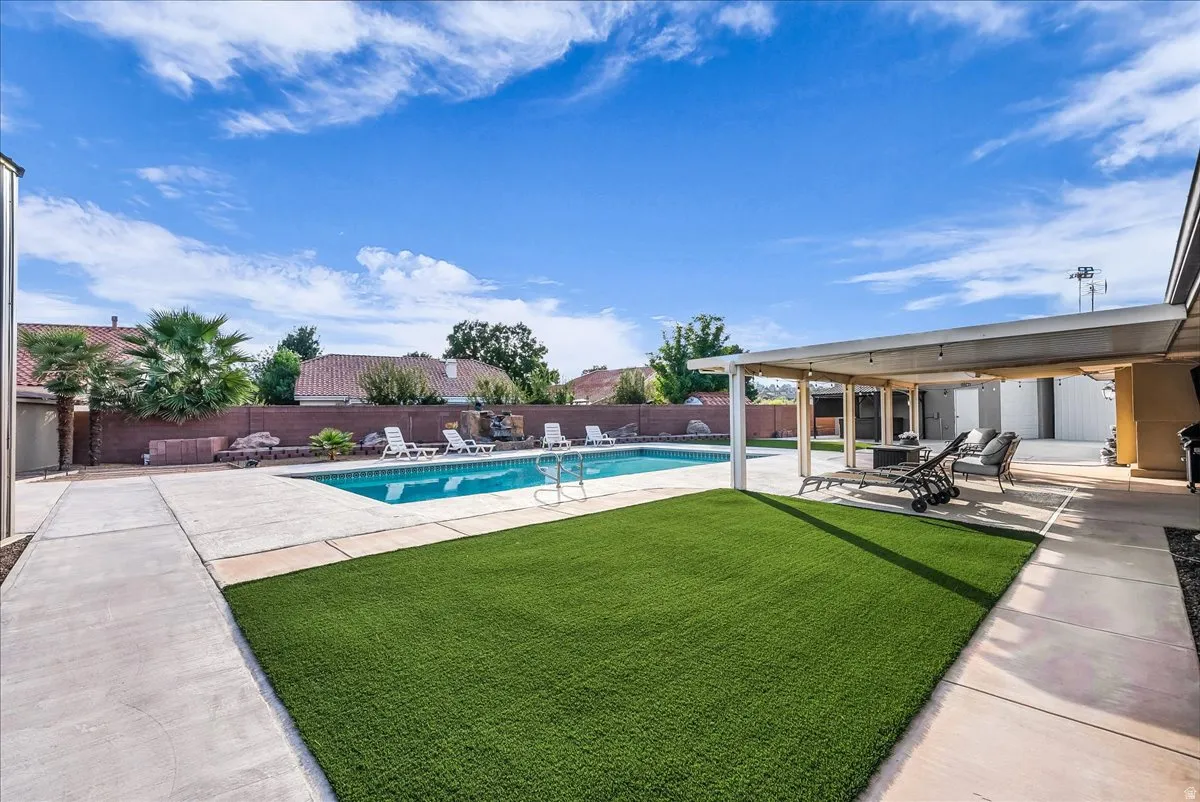 Swimming pool with integrated waterfall feature, artificial turf area, concrete patio, and a covered outdoor living space