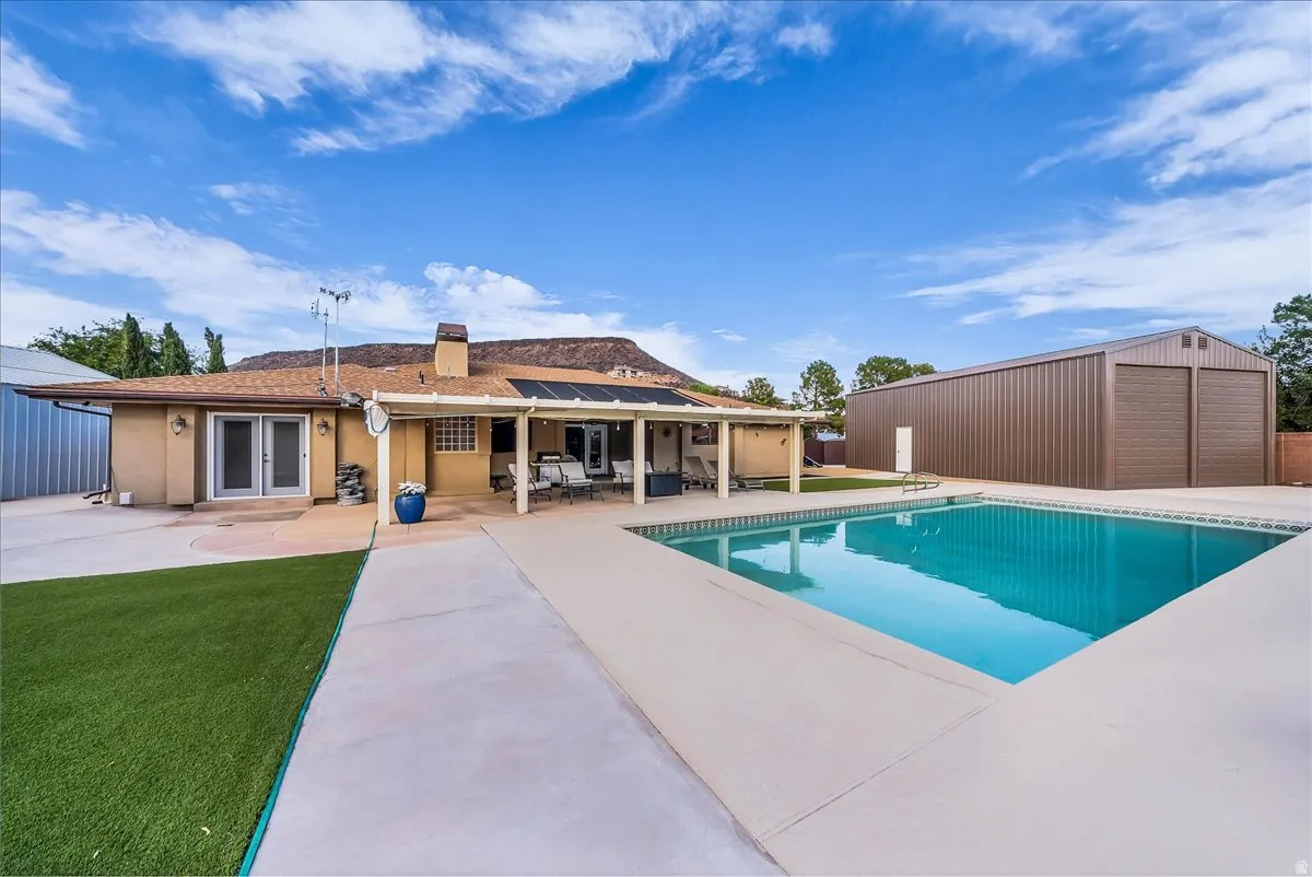 Expansive outdoor space featuring a rectangular swimming pool, concrete patio, and a large metal outbuilding with two garage doors