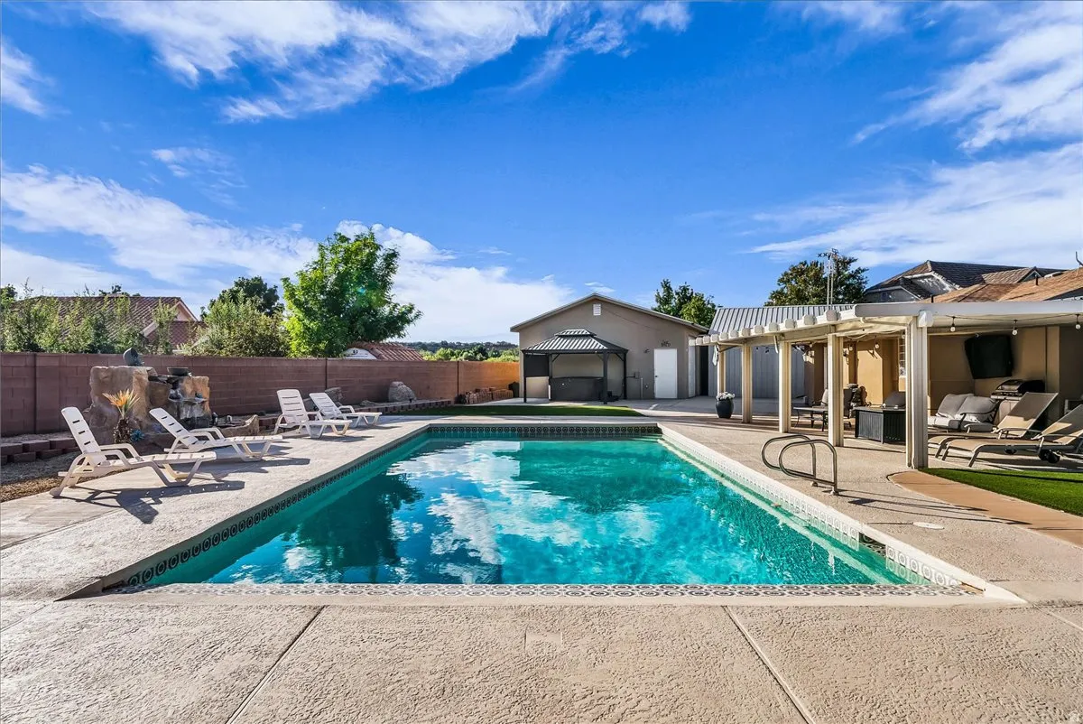 Rectangular swimming pool with integrated steps, concrete pool deck, attached pergola, and a detached structure with an additional covered patio