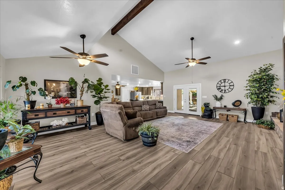 Vaulted ceiling with exposed wood beam, wood-finish flooring, recessed lighting, and dual ceiling fans