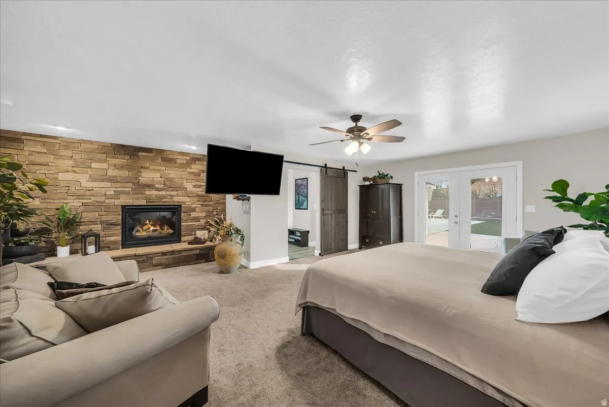 Stone-clad fireplace with a hearth, ceiling fan, double French doors, and a wood-finish barn door