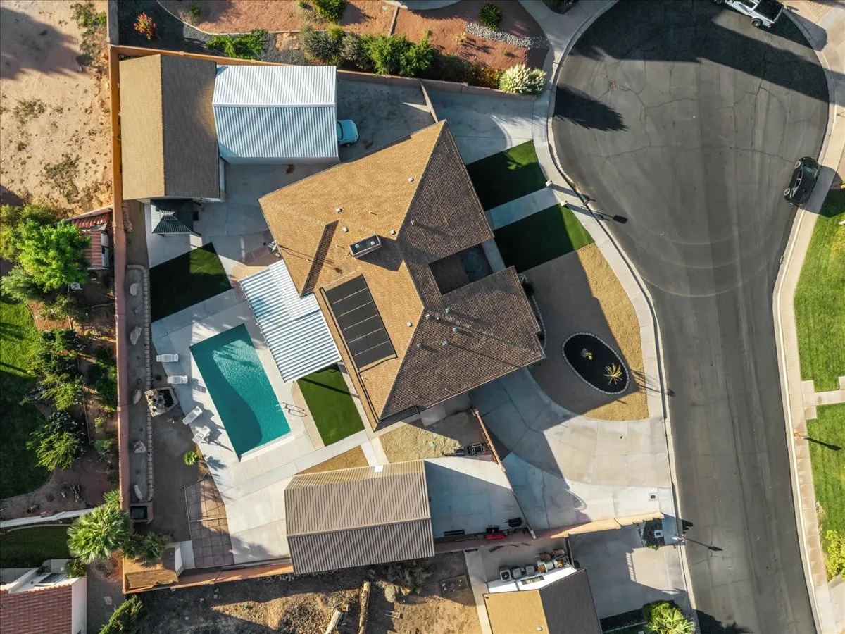 Swimming pool with concrete surround, synthetic turf accents, solar panels, and a detached auxiliary structure