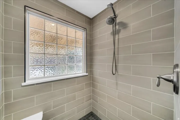 Glass block window with white trim, subway tile walls, dark-toned floor tile, and a brushed nickel shower fixture