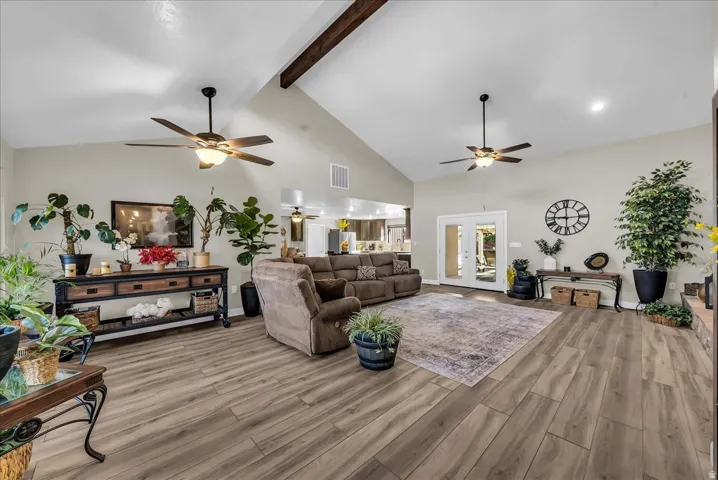 Vaulted ceiling with exposed wood beam, wood-finish flooring, recessed lighting, and dual ceiling fans