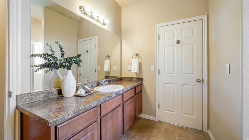 Vanity with an integrated sink, laminate countertop, wood-finish cabinetry, and a mirrored wall