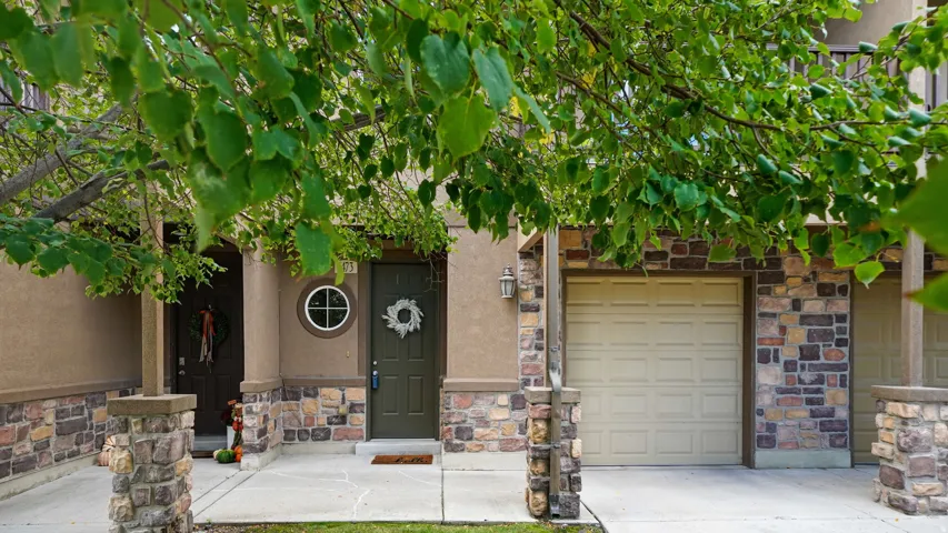 Stucco exterior with stone veneer accents, an attached garage, a front entry door with a circular window, and concrete pathways