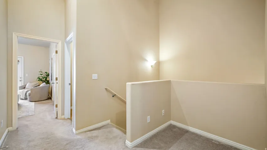 Carpeted hallway with a staircase, featuring a wall-mounted sconce and a wood handrail