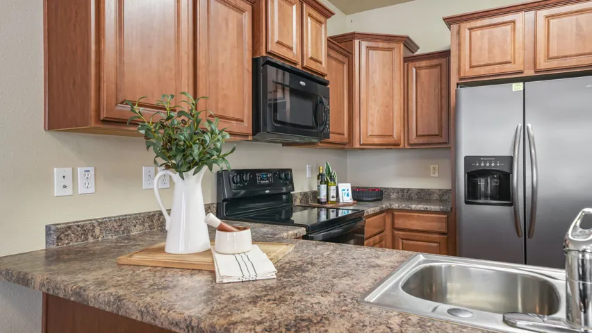 Kitchen featuring wood cabinetry, mottled countertops, stainless steel side-by-side refrigerator, black electric range, and integrated stainless steel sink