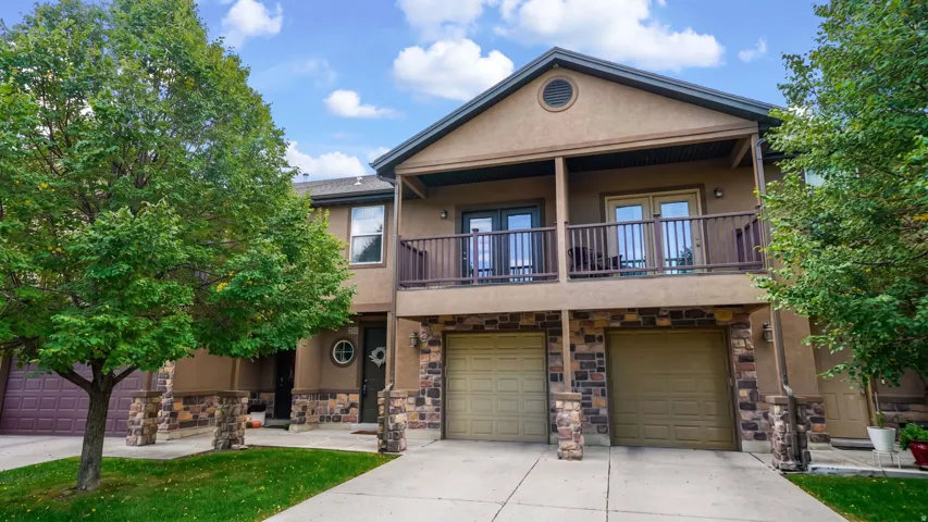 Stucco exterior with stone accents, dual two-car garages, and an upper-level balcony with French doors