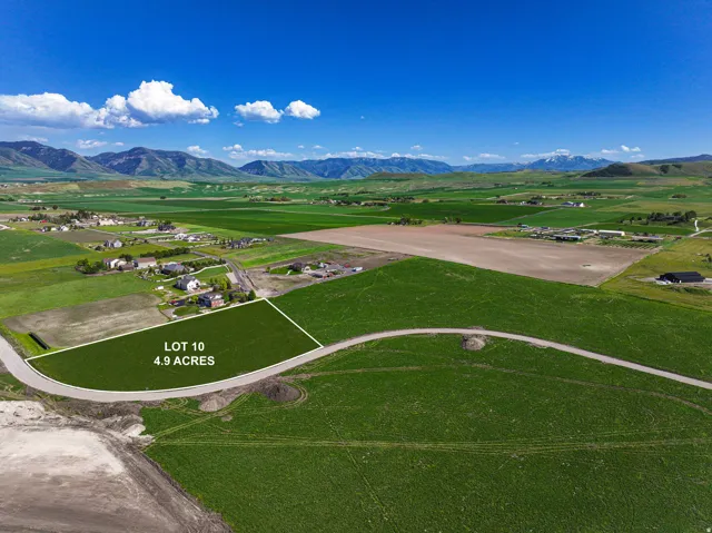 4.9-acre Lot 10 featuring expansive green fields, a paved road frontage, and distant mountain backdrops