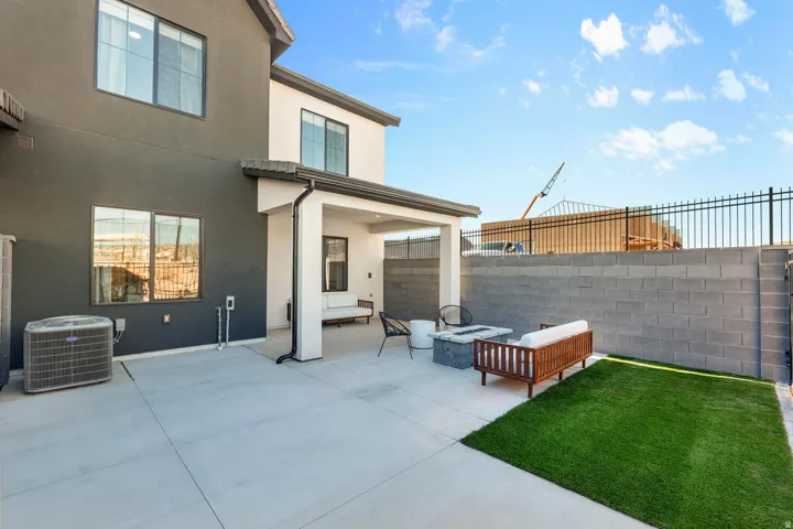 Expansive concrete patio with a covered outdoor area, a low stone fire pit, and an artificial turf lawn