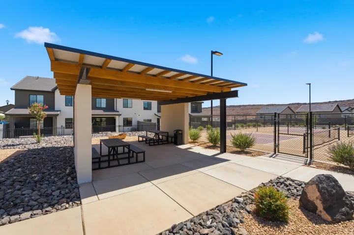 Covered patio with integrated seating, concrete flooring, and an adjacent fenced sports court